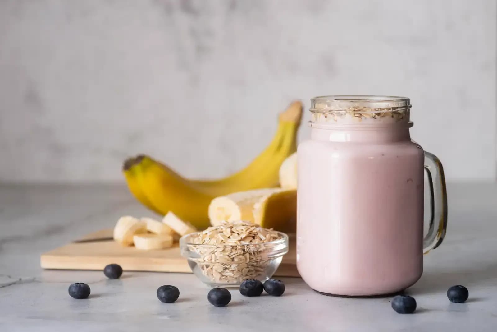 A smoothie with some potential ingredients in the background, including some blueberries and cut up bananas