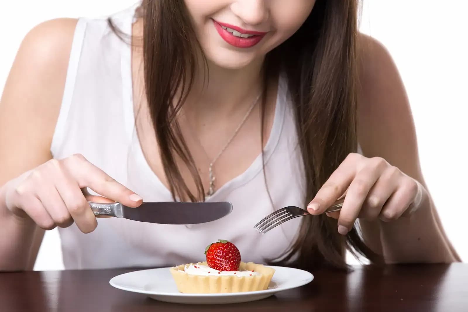 A smiling woman holding a knife and fork looking excitedly at her meal