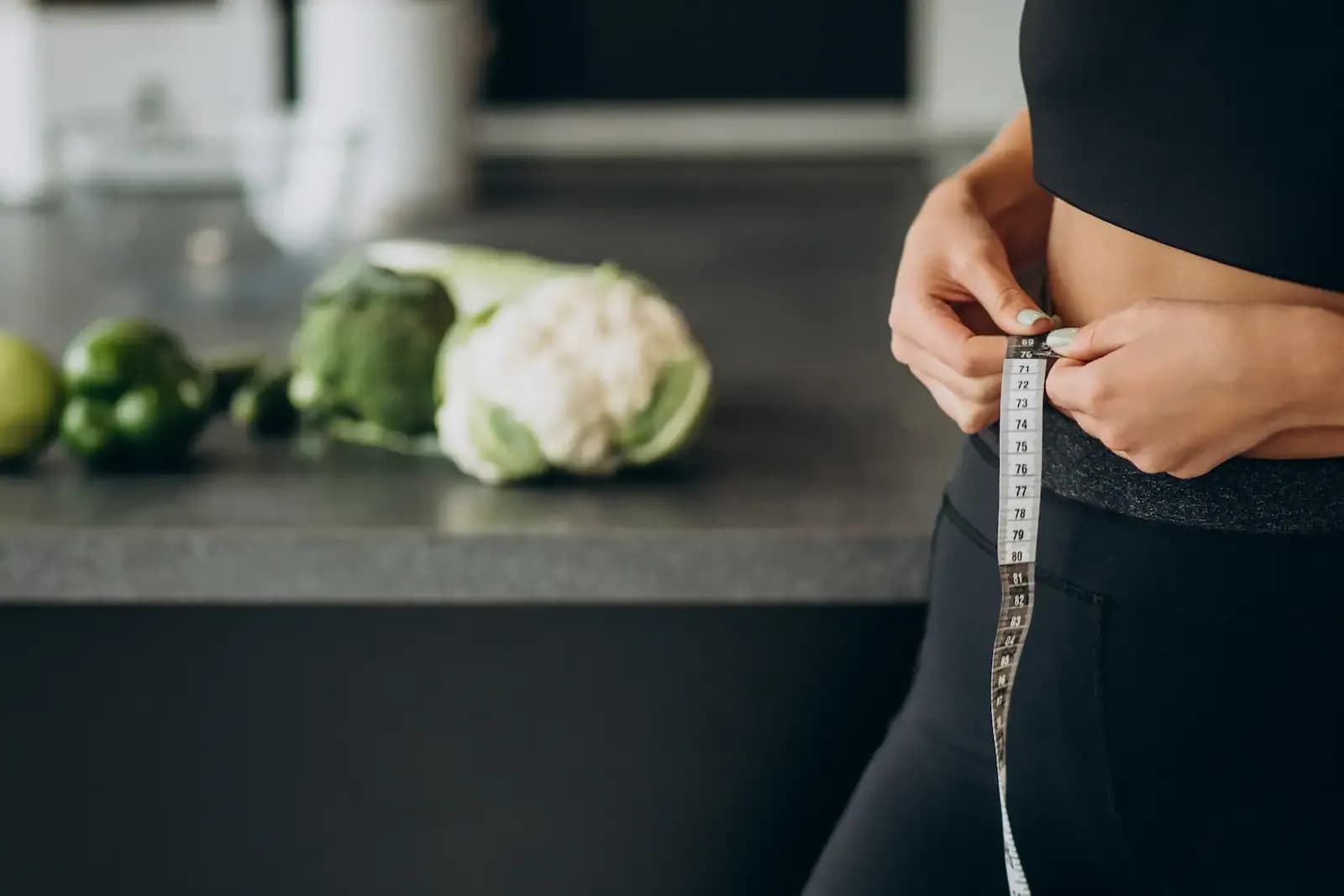 A young woman in her kitchen using measuring tape to find her waistline