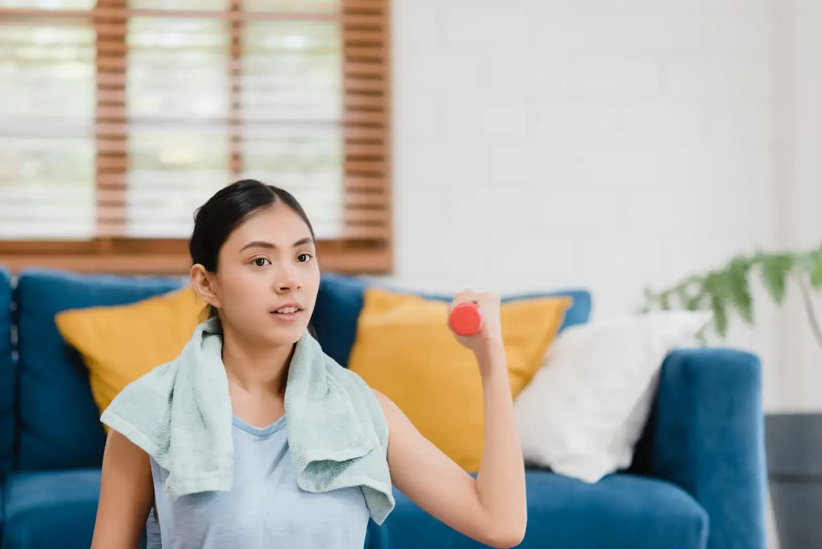 A young woman with a towel around her neck working out from her living room by lifting weights